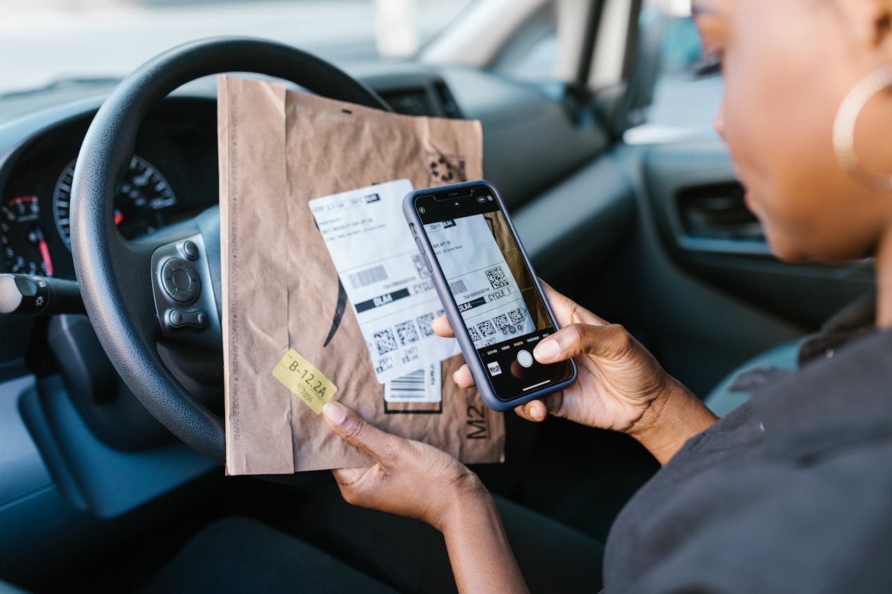 Close-up of a courier in a car scanning a package label with a smartphone for delivery service.